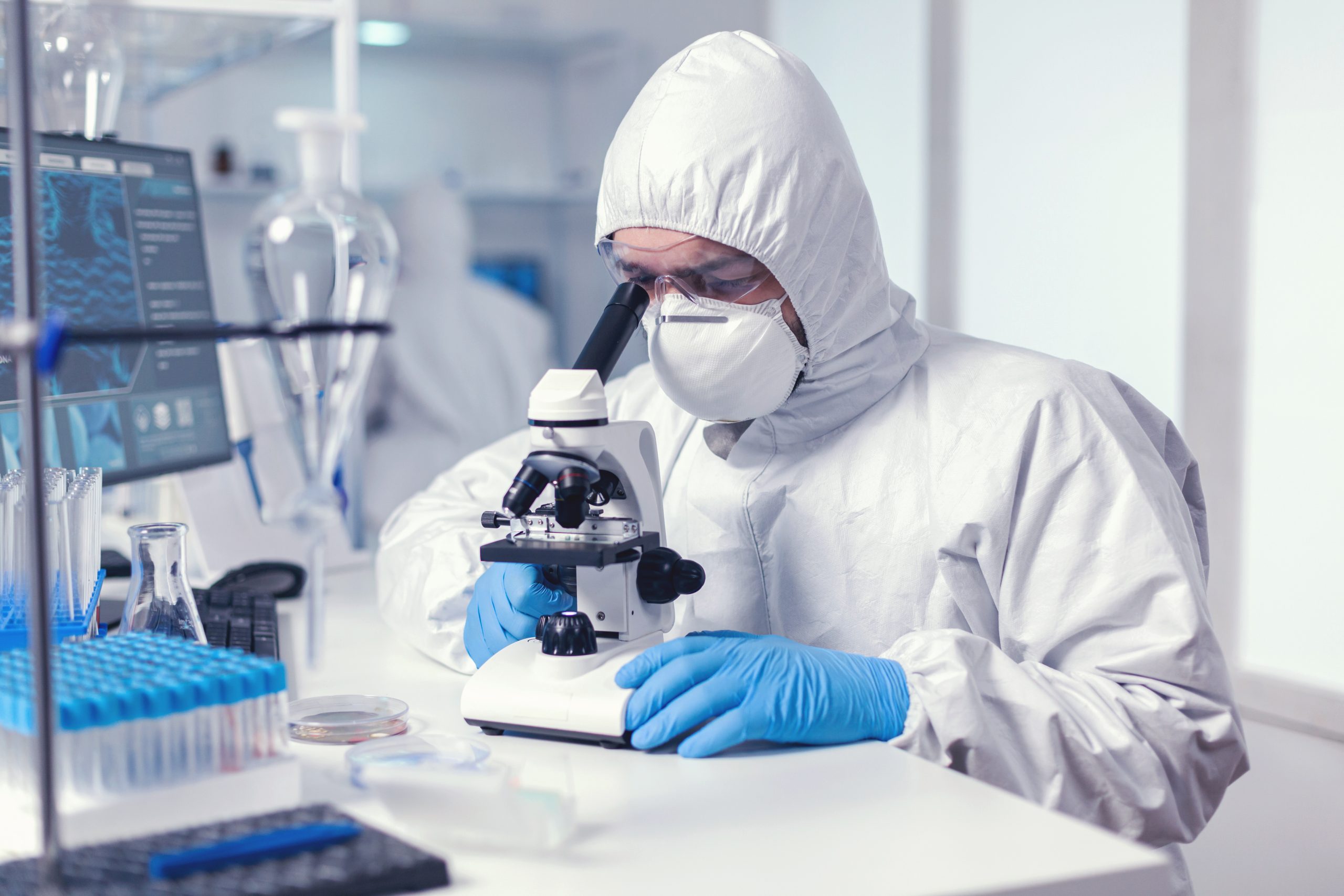 microbiologist-with-protection-glasses-using-microscope-dressed-ppe-suit-scaled